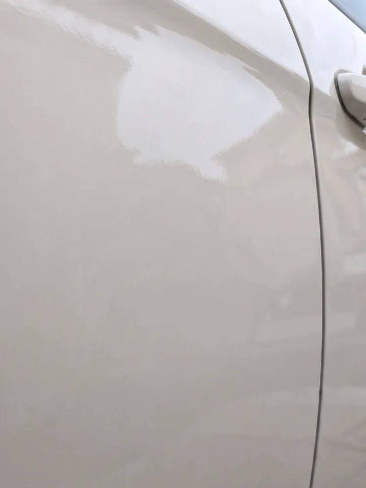 Après débosselage sans peinture : panneau de portière blanc remis à plat, surface lisse aux reflets continus