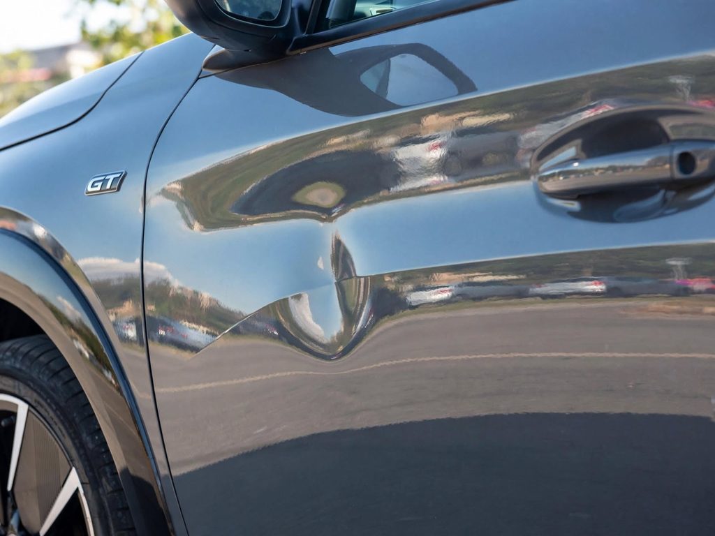 Bosse de parking sur la portière d'une voiture grise en ville : enfoncement net de la tôle, peinture intacte