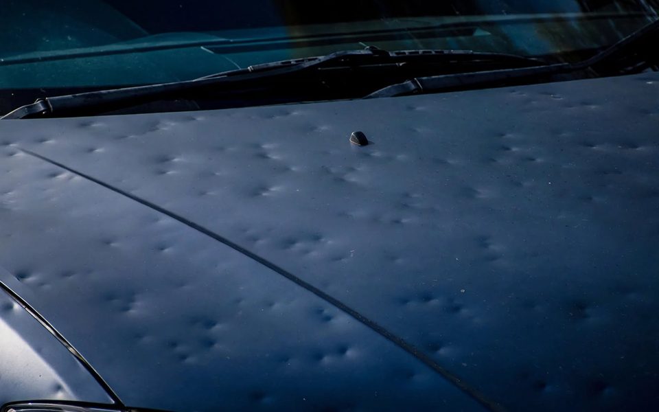 Avant débosselage sans peinture : capot de voiture couvert d'impacts de grêle, pris en charge en sous-traitance pour garage