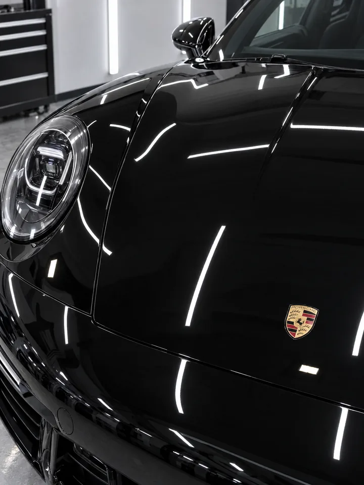 Après polissage : capot de Porsche 911 noire à la brillance miroir, reflets nets et tranchés